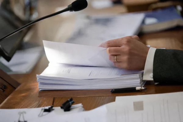 Dossier de commission et micro de séance sur une table, avec mains anonymes et documents flous en lumière naturelle.