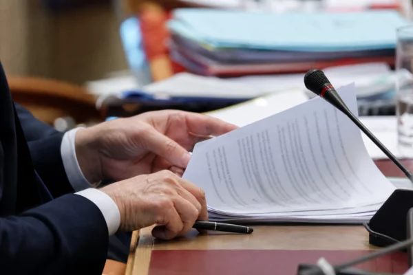 Mains anonymes feuilletant un dossier devant un micro de commission dans un cadre institutionnel français