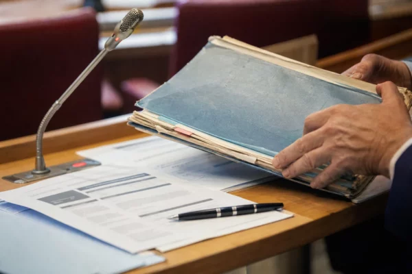 Mains anonymes consultant un dossier flou près d’un micro de commission dans une salle institutionnelle française