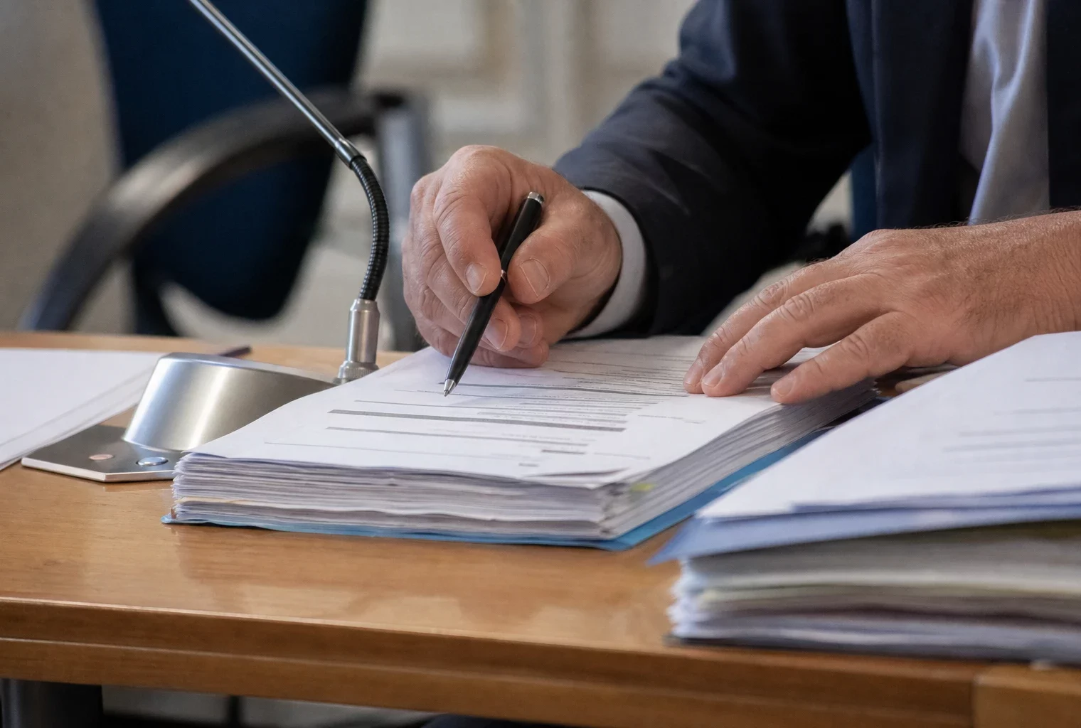 Mains anonymes examinant un dossier flou près d’un micro lors d’une audition publique à Rennes
