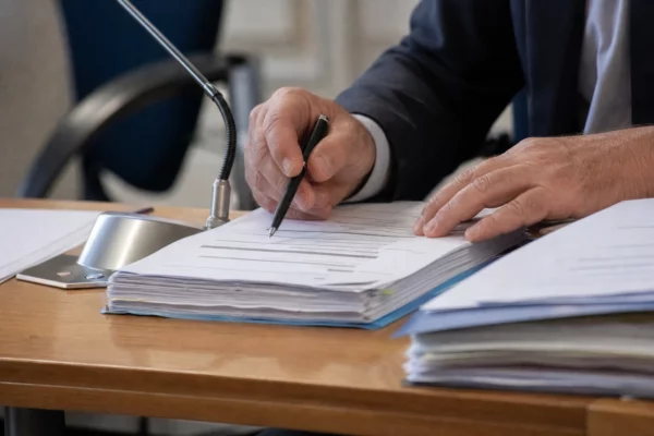 Mains anonymes examinant un dossier flou près d’un micro lors d’une audition publique à Rennes