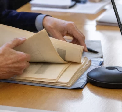 Mains anonymes examinant un dossier d’audition près d’un micro de commission, dans une lumière naturelle claire