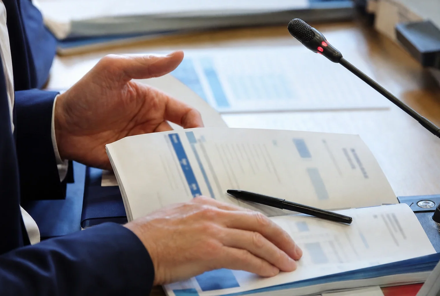 Mains anonymes examinant un dossier environnemental près d’un micro de commission parlementaire français