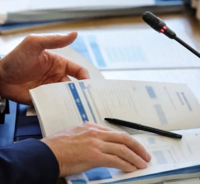 Mains anonymes examinant un dossier environnemental près d’un micro de commission parlementaire français