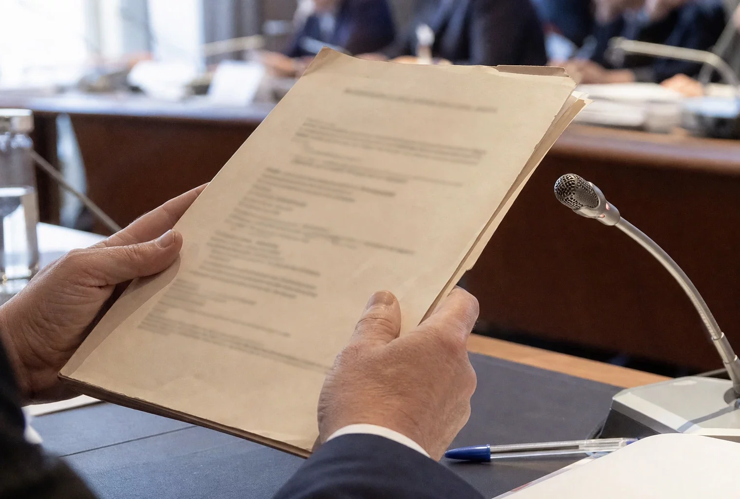 Mains anonymes tenant un dossier devant un micro de commission lors d’une audition judiciaire en France
