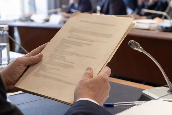 Mains anonymes tenant un dossier devant un micro de commission lors d’une audition judiciaire en France