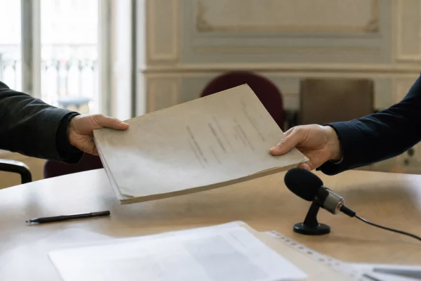 Mains anonymes transmettant un dossier de candidature près d’un micro de commission, dans une institution française