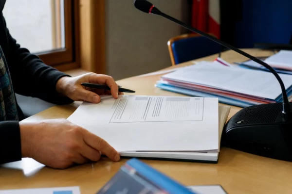 Mains anonymes examinant un dossier de recrutement près d’un micro dans une mairie française