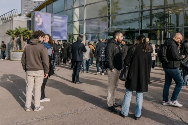 Scène de rue devant une salle événementielle parisienne, avec des participants anonymes et des palmiers en arrière-plan.