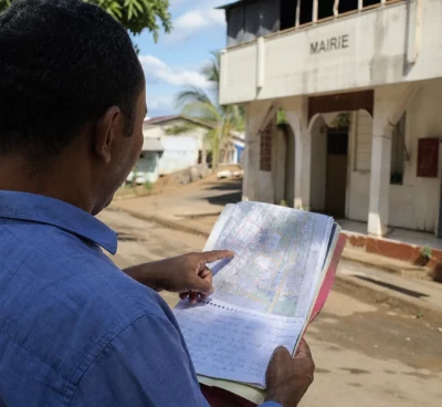 Élu local anonyme consultant un dossier de reconstruction devant une mairie à Mayotte, sous une lumière claire
