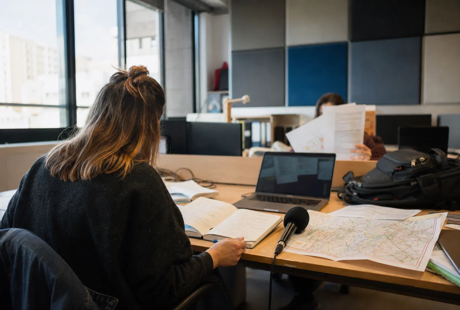 Journaliste préparant une enquête locale dans une rédaction française, avec carnet, micro et carte floue sur le bureau