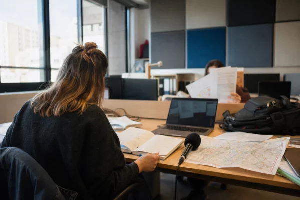 Journaliste préparant une enquête locale dans une rédaction française, avec carnet, micro et carte floue sur le bureau