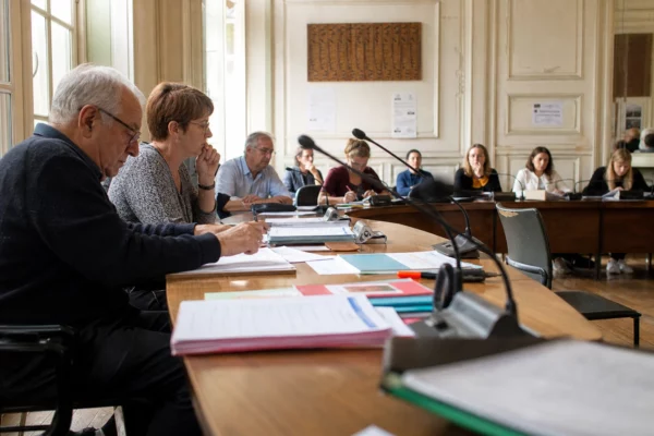 Salle municipale française avec élus anonymes, micros et une chaise vide lors d’une réunion sur les familles monoparentales