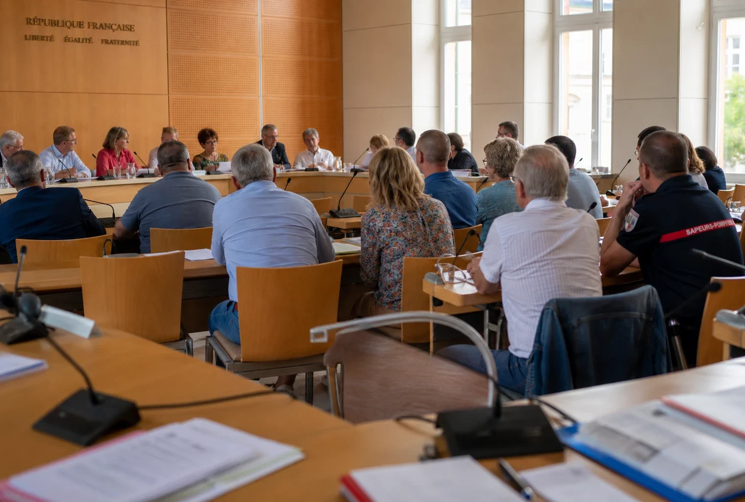 Salle municipale française avec chaise vide, micros et dossiers lors d’un débat sur le financement des pompiers