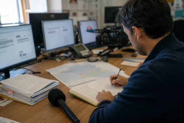 Journaliste préparant une analyse politique dans une rédaction locale, avec carnet, carte floue et micro de presse