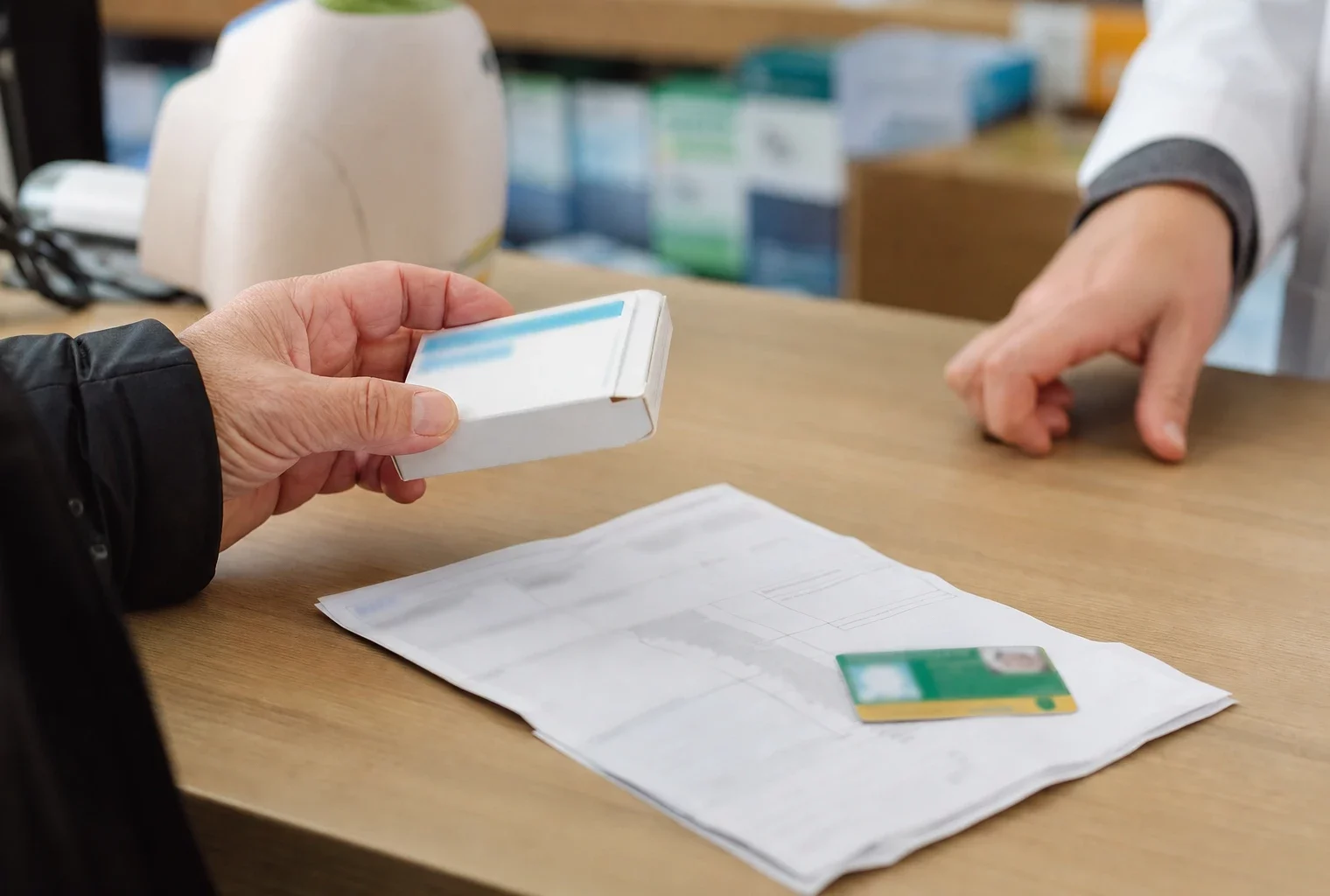 Main d’un patient tenant une boîte de médicaments et une ordonnance sur le comptoir d’une pharmacie française