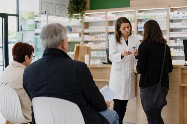 Patient échangeant avec un pharmacien dans une salle d’attente claire d’une pharmacie française