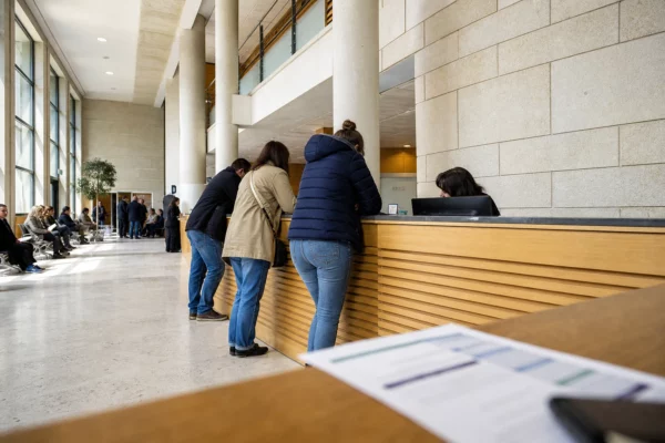 Hall lumineux d’un service public de santé où des patients anonymes échangent au comptoir d’accueil