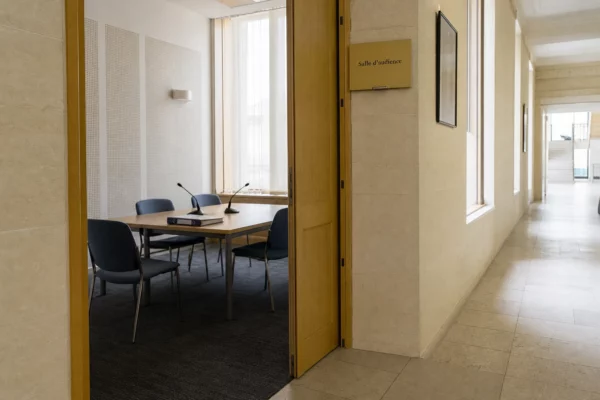 Couloir clair d’une institution publique française avec salle d’audition et dossiers anonymes sur une table