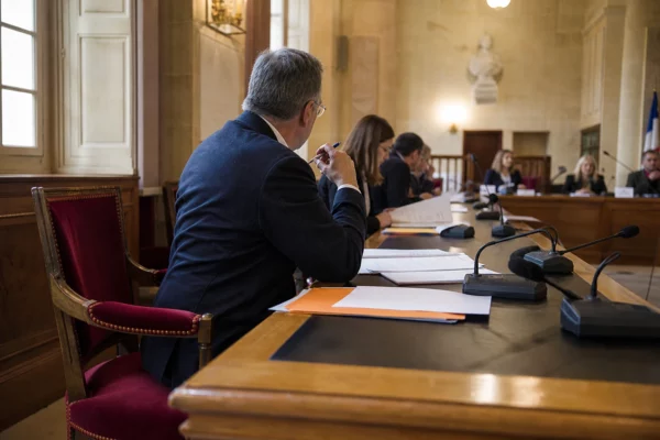 Salle municipale lumineuse avec chaise vide, micros et dossiers flous lors d’une réunion politique locale.