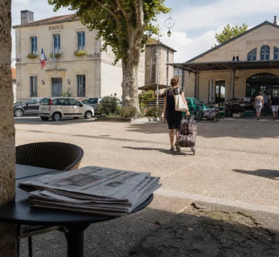 Place de village en Gironde avec habitants anonymes, mairie en arrière-plan et ambiance de retour à la normale.