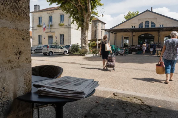 Place de village en Gironde avec habitants anonymes, mairie en arrière-plan et ambiance de retour à la normale.