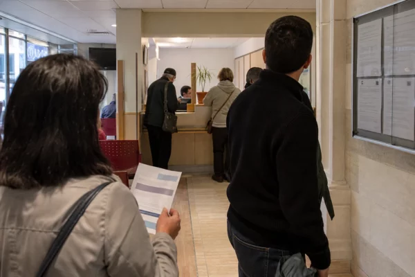 Des usagers anonymes dans un hall de service public français consultent un document de campagne flouté.