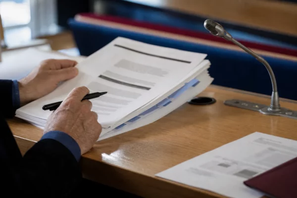 Mains anonymes examinant un dossier d’élu local avec un micro de commission et un stylo, dans une salle claire