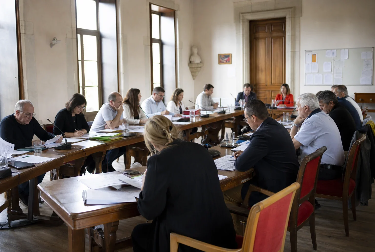 Salle de conseil municipal française avec micros, dossiers flous et une chaise vide pendant une réunion politique