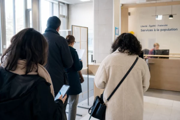 Hall lumineux d’un service public français avec usagers anonymes, smartphone à l’écran flou et affichage institutionnel hors focus.