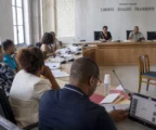Salle municipale française avec élus anonymes, chaise vide et micros lors d’un débat sur les ingérences numériques