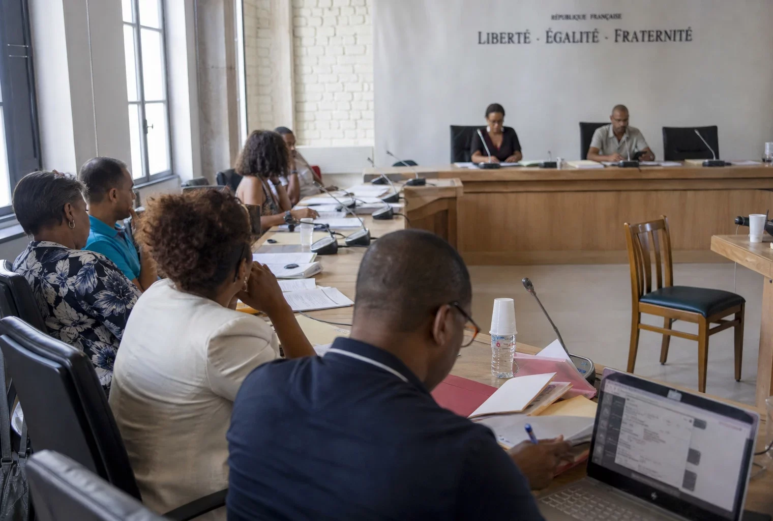 Salle municipale française avec élus anonymes, chaise vide et micros lors d’un débat sur les ingérences numériques