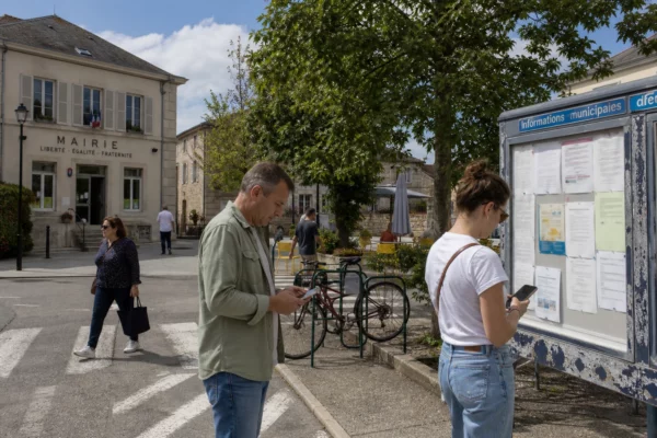 Habitants anonymes d’une ville française consultant leur téléphone près d’une mairie et d’un panneau public
