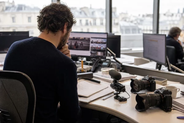 Reporter dans une rédaction française avec écrans flous, caméra et micro, dans une ambiance de presse claire et réaliste.