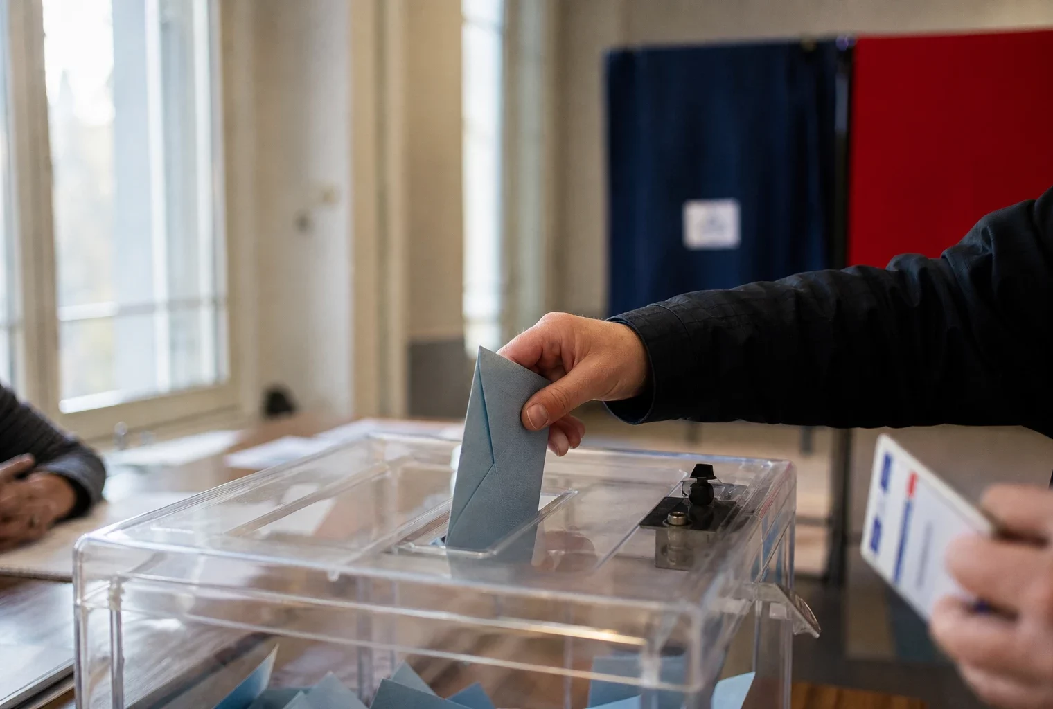 Main anonyme déposant un bulletin dans une urne transparente lors d’un vote dans un bureau français