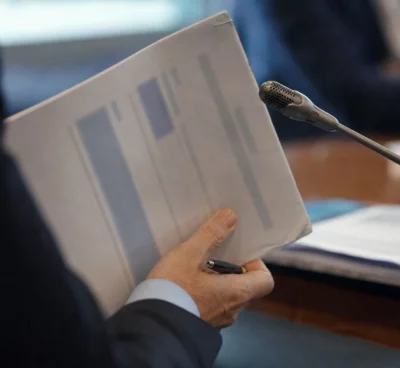 Mains anonymes tenant un dossier lors d’une audition, avec micro de commission et documents flous
