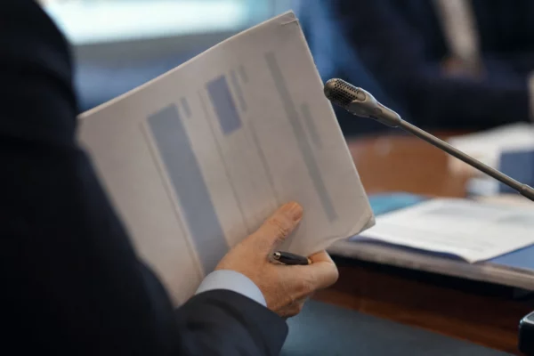 Mains anonymes tenant un dossier lors d’une audition, avec micro de commission et documents flous