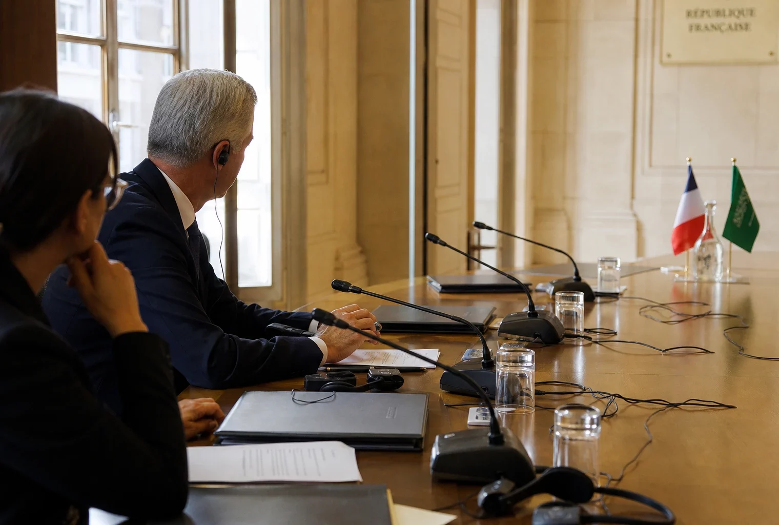 Table de négociation franco-saoudienne avec micros, écouteurs et dossiers dans une salle institutionnelle française