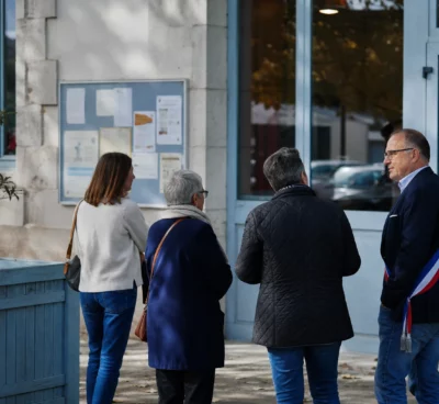 Des citoyens et un élu local près d’une mairie, dans une scène de vie civique française en lumière naturelle.