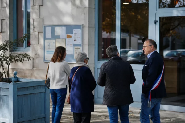Des citoyens et un élu local près d’une mairie, dans une scène de vie civique française en lumière naturelle.