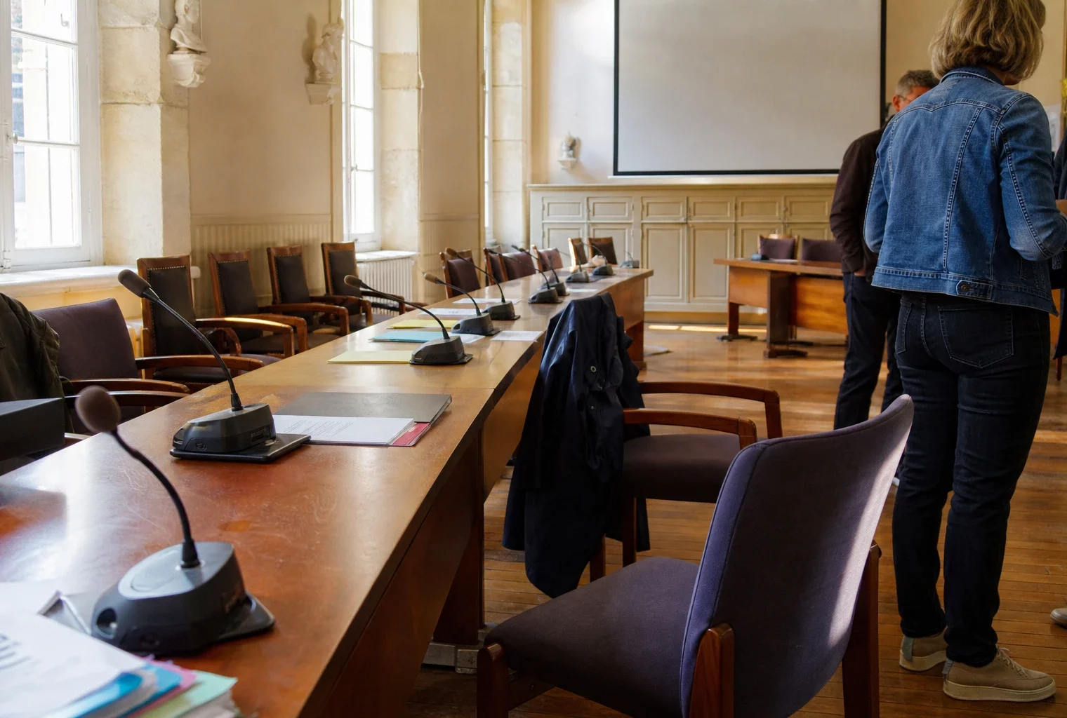 Salle municipale lumineuse avec micros, dossiers et chaises vides après une réunion sur la reconstruction post-incendie.