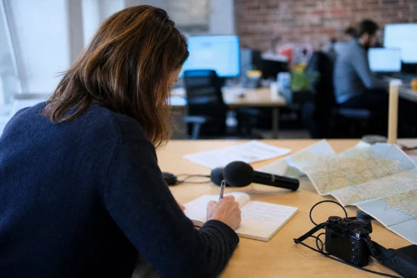 Journaliste préparant un sujet politique dans une rédaction locale, avec carnet, micro et carte régionale floue