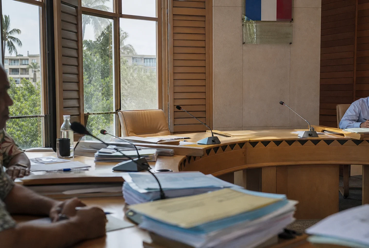 Salle du conseil à Nouméa avec chaise vide, micros et dossiers, dans une ambiance institutionnelle claire et sobre.