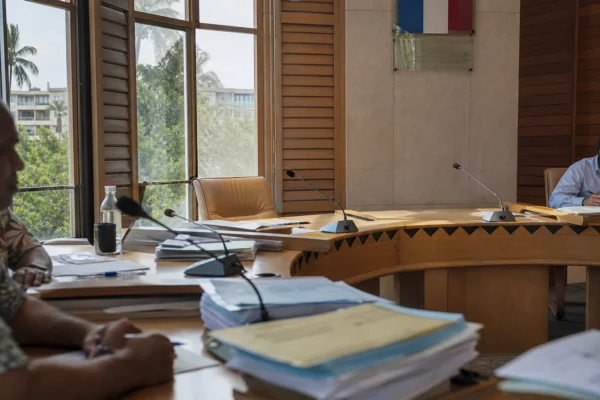 Salle du conseil à Nouméa avec chaise vide, micros et dossiers, dans une ambiance institutionnelle claire et sobre.