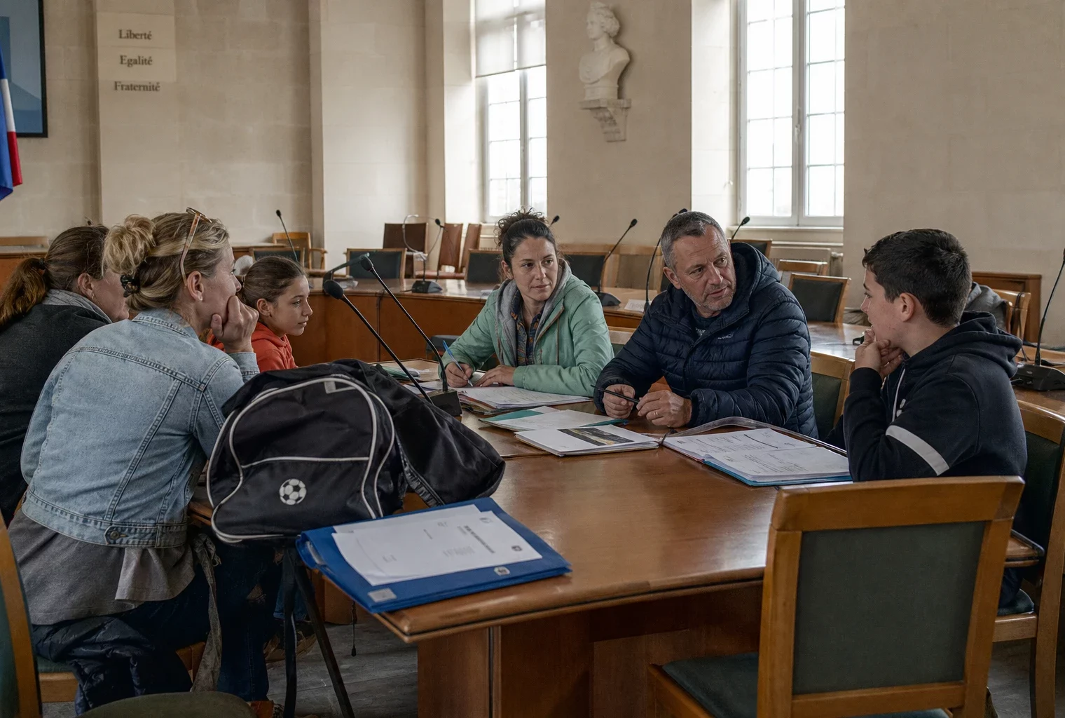 Réunion dans une salle municipale autour du pass Sport, avec jeunes, parents, micros et dossiers sur une table