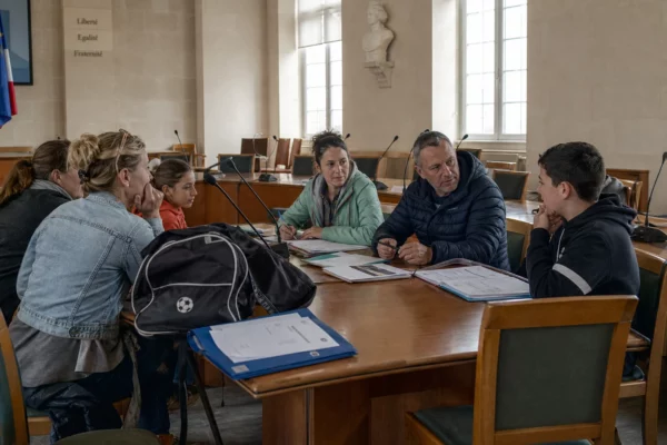 Réunion dans une salle municipale autour du pass Sport, avec jeunes, parents, micros et dossiers sur une table