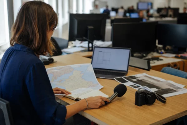 Journaliste préparant un sujet sur le piratage fiscal dans une rédaction française, avec micro et carte floue