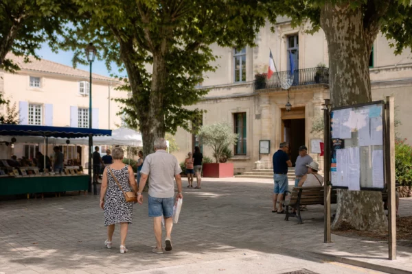 Place de petite ville française en été, devant la mairie, avec habitants anonymes et ambiance de reportage local.