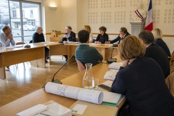 Réunion d’un conseil municipal français sur la gestion de l’eau, avec micros, dossiers et une chaise vide