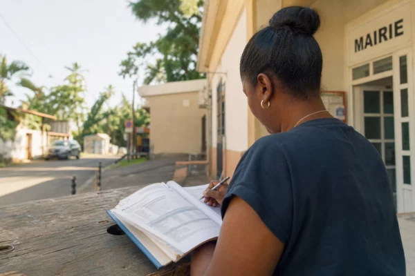 Portrait d’un élu local anonyme à Mayotte prenant des notes devant une mairie, dans une lumière tropicale claire